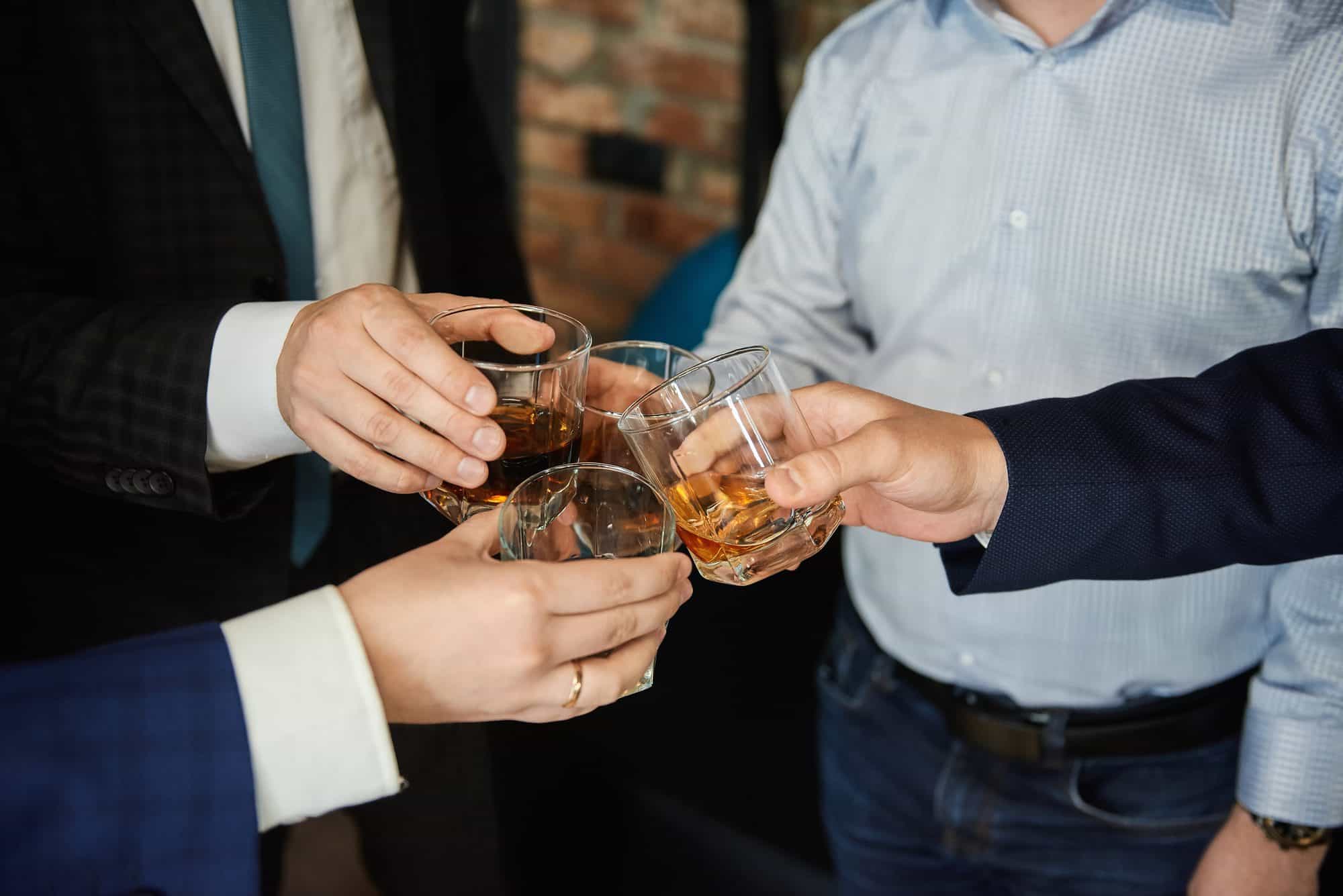 Group of four friends men in the whisky drink party holding glass of alcoholic beverages in their hands and clinking. Close up